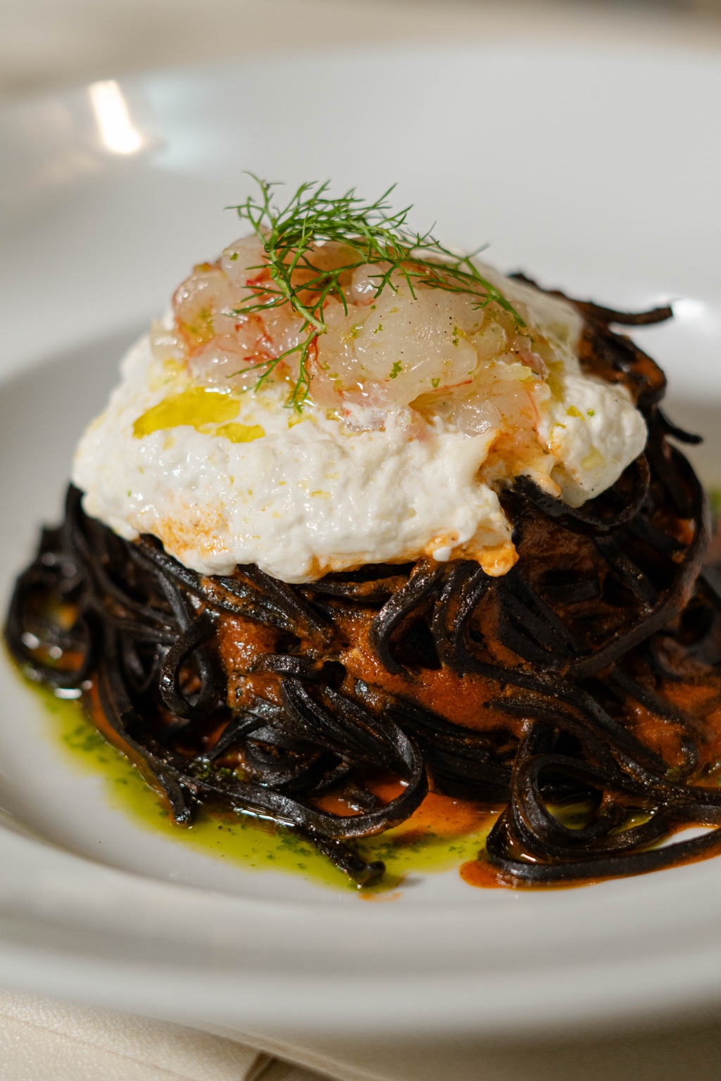 Pasta scura con crema e tartare, impiattata su un piatto bianco